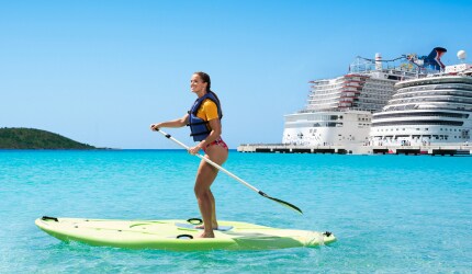 lady paddleboarding in crystal clear water with two carnival ships in the background