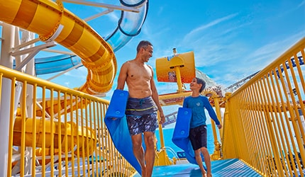 father and son walking to the entrance of the waterslides with holding floats