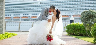 a man and a woman posing for a photo after their wedding with carnival ship in the background