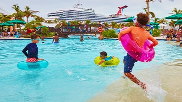 kids enjoying the pool with floats and a carnival cruise ship in the background