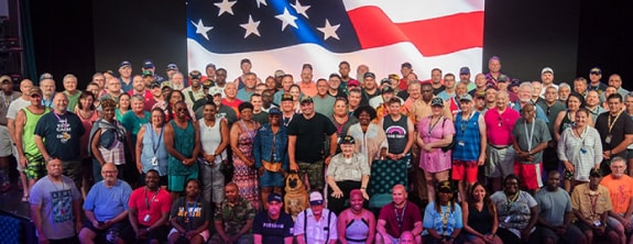 a group of military guests pose for a photo on stage with the american flag in the background